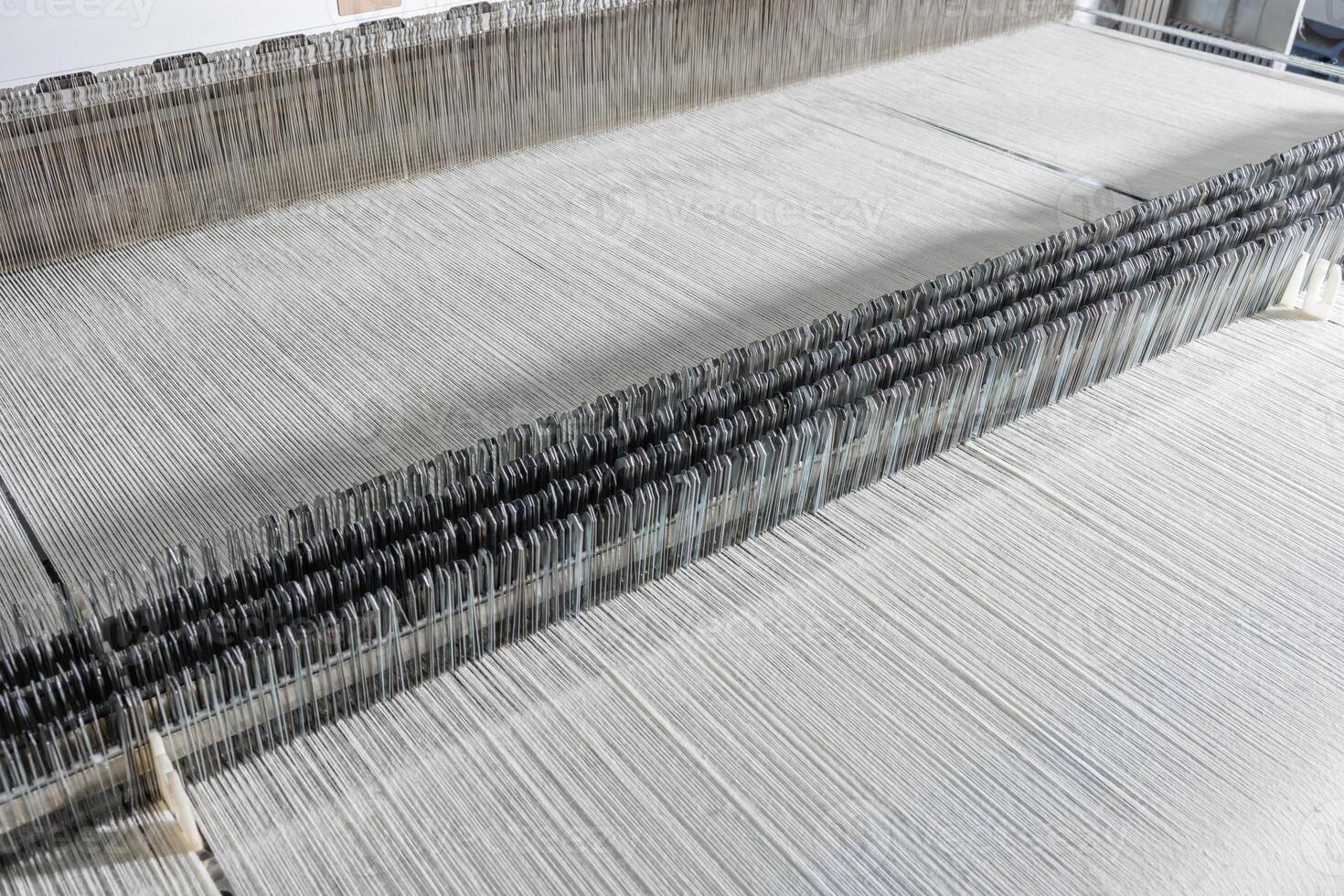 Weaving loom with fine threads in textile mill, industrial close-up of fabric manufacturing process. photo