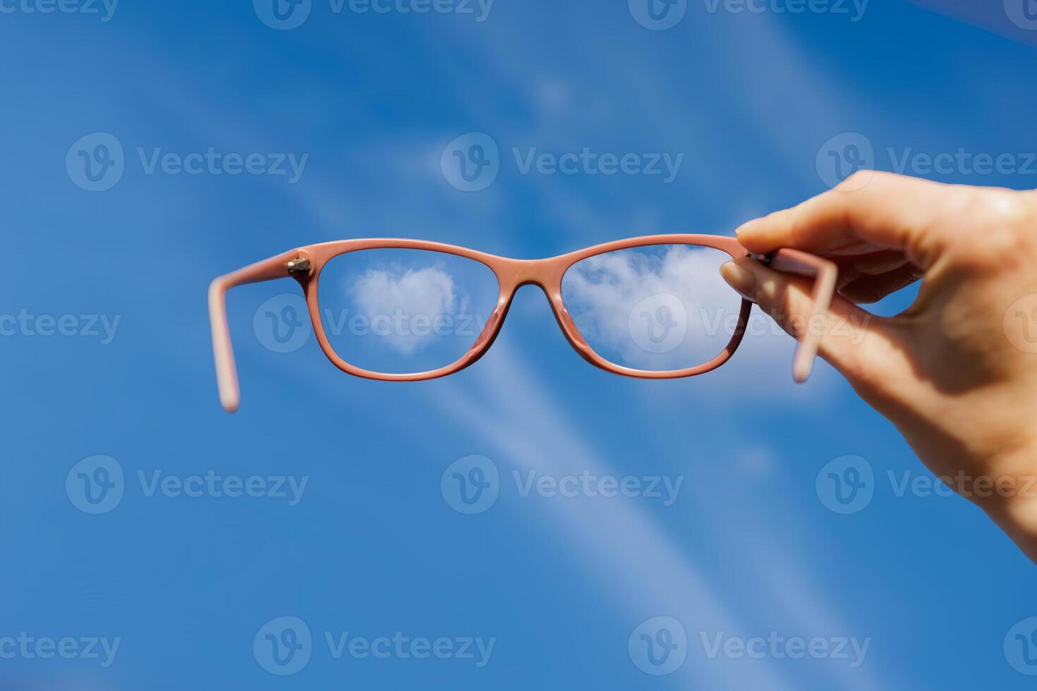 Eyeglasses held up against a bright blue sky, reflecting clouds through clear lenses. Concept of clarity, vision improvement, optimism, and fresh perspective on life. photo