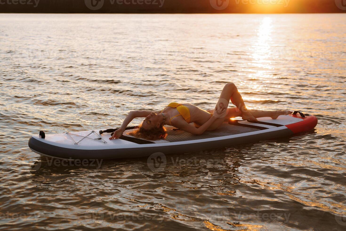 girl in swimsuit relaxes lying on Sup boarding in the rays of warm sunset sun, active recreation photo