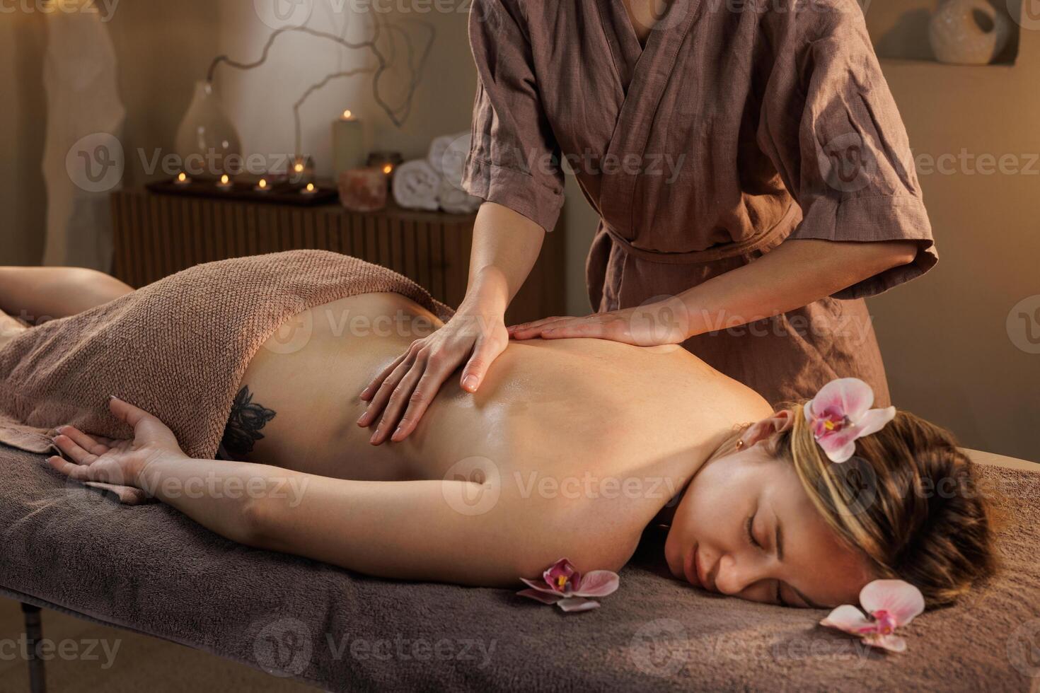 Close-up of professional back massage in serene spa setting with flowers, soft lighting, and therapist hands promoting relaxation, healing, and skin rejuvenation. photo