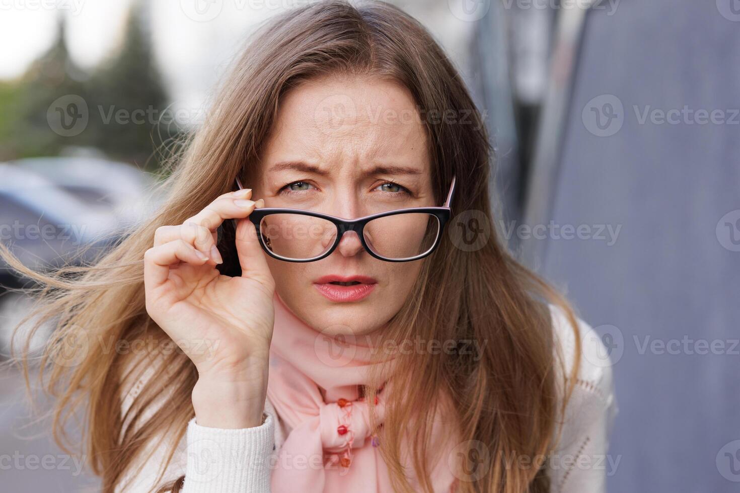 Portrait of a young woman squinting and holding glasses while trying to see clearly, representing poor vision, blurred eyesight, or difficulty focusing in everyday life. photo