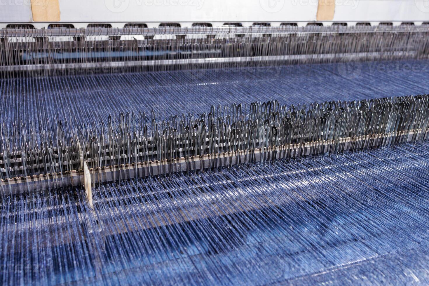 Automated loom weaving blue textile, detailed view of industrial warp threads and heddles. photo
