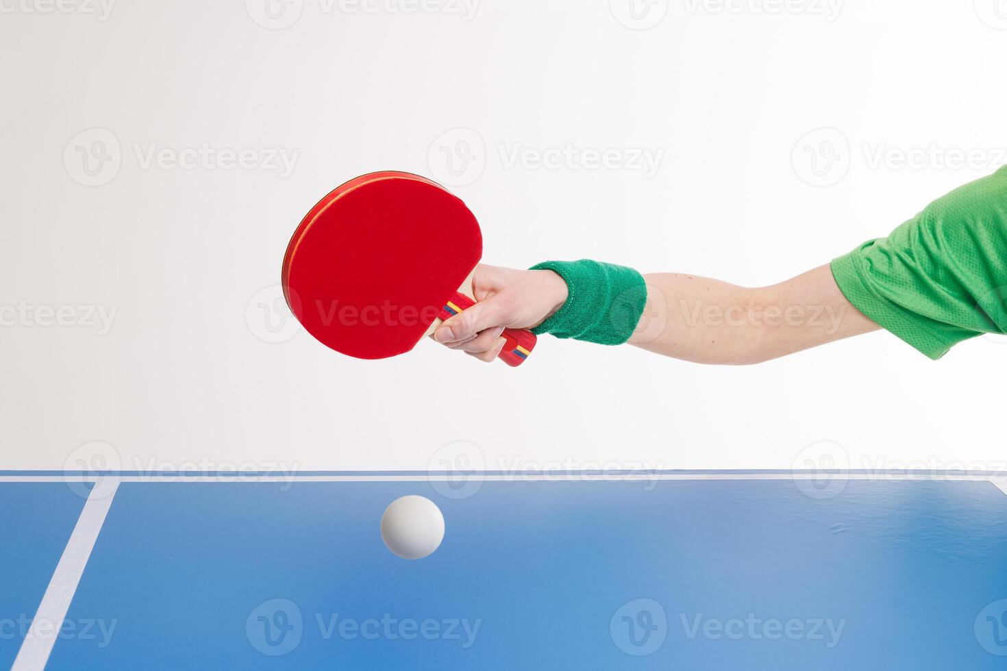 Hand with red paddle hits white ping pong ball over blue table. photo