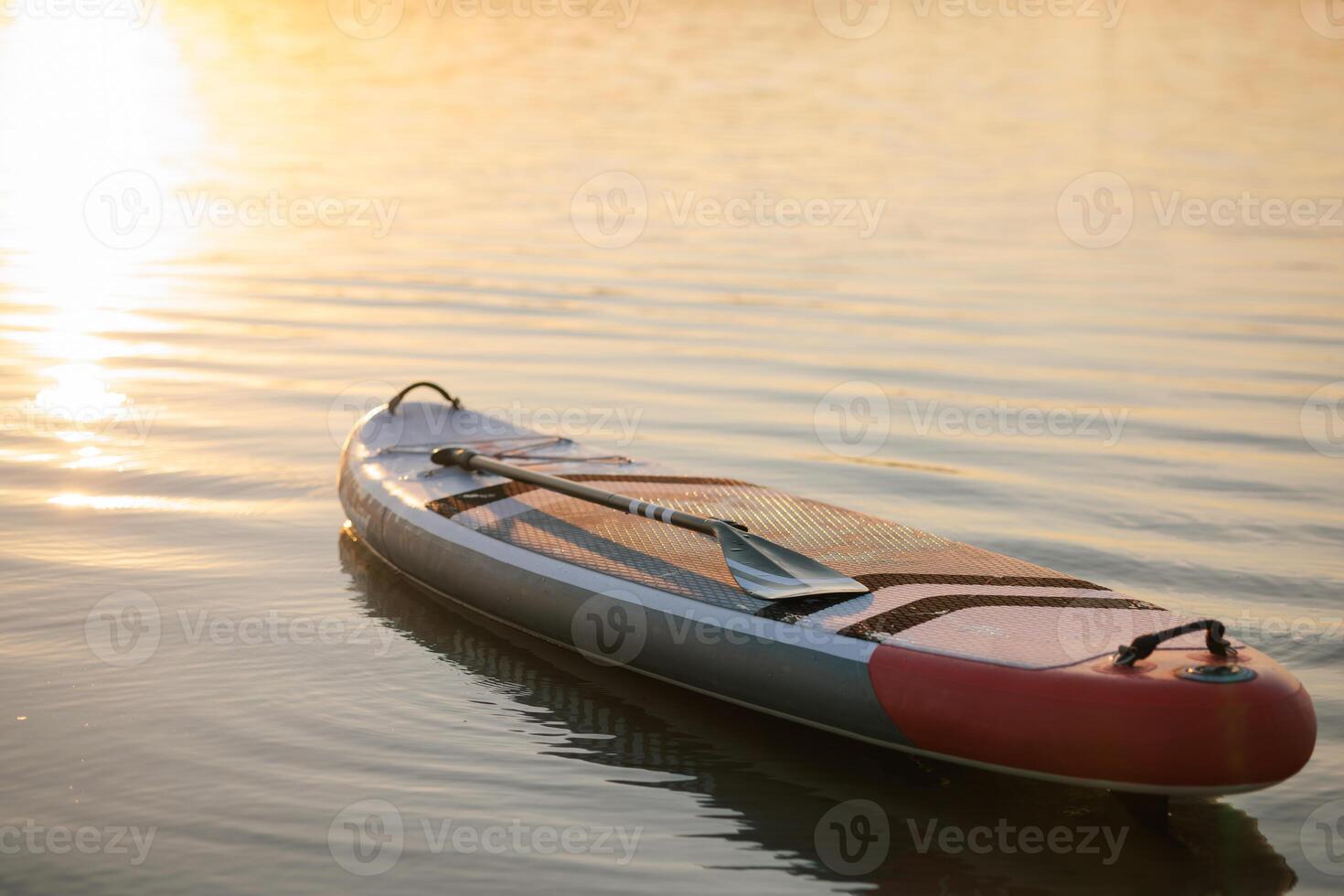 Stand up paddleboard with paddle floating alone on calm lake during golden sunset, evoking peaceful solitude, outdoor adventure, and summer relaxation. photo