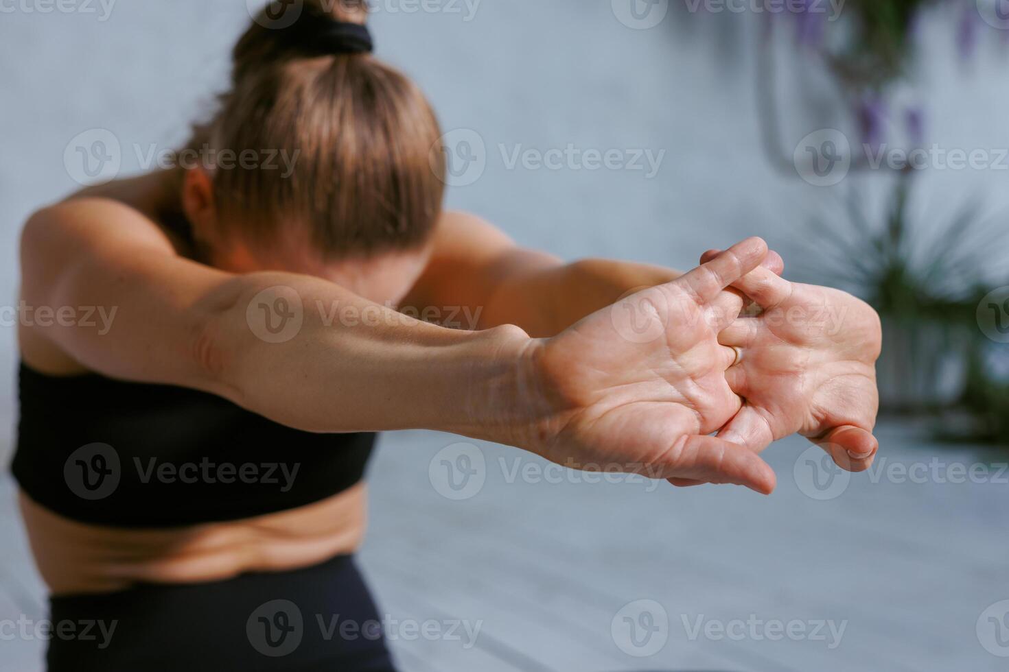 Close-up of woman in black sportswear stretching her arms forward during yoga practice indoors, focusing on flexibility, relaxation, and mindful movement for a healthy and balanced lifestyle. photo