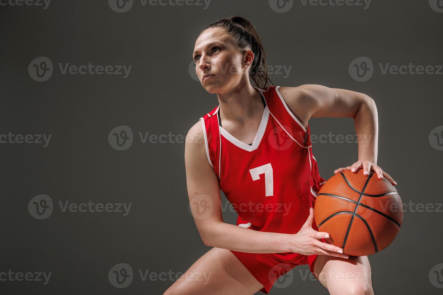 Focused Female Basketball Player in Red Uniform Holding Ball, Ready for Action on Dark Background photo