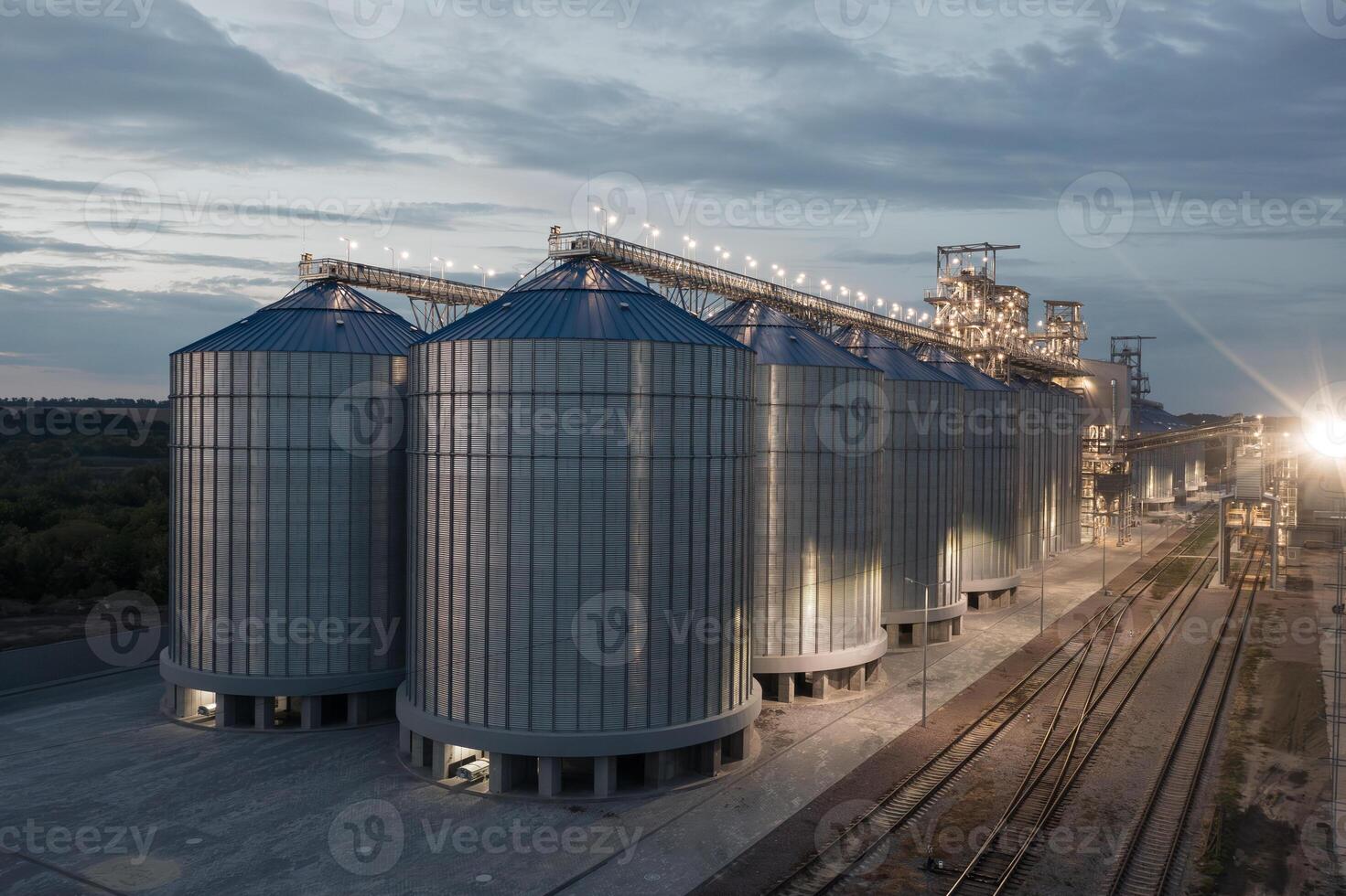 Illuminated Grain Silos and Industrial Elevator at Night with Railway Tracks Modern Agriculture Concept photo