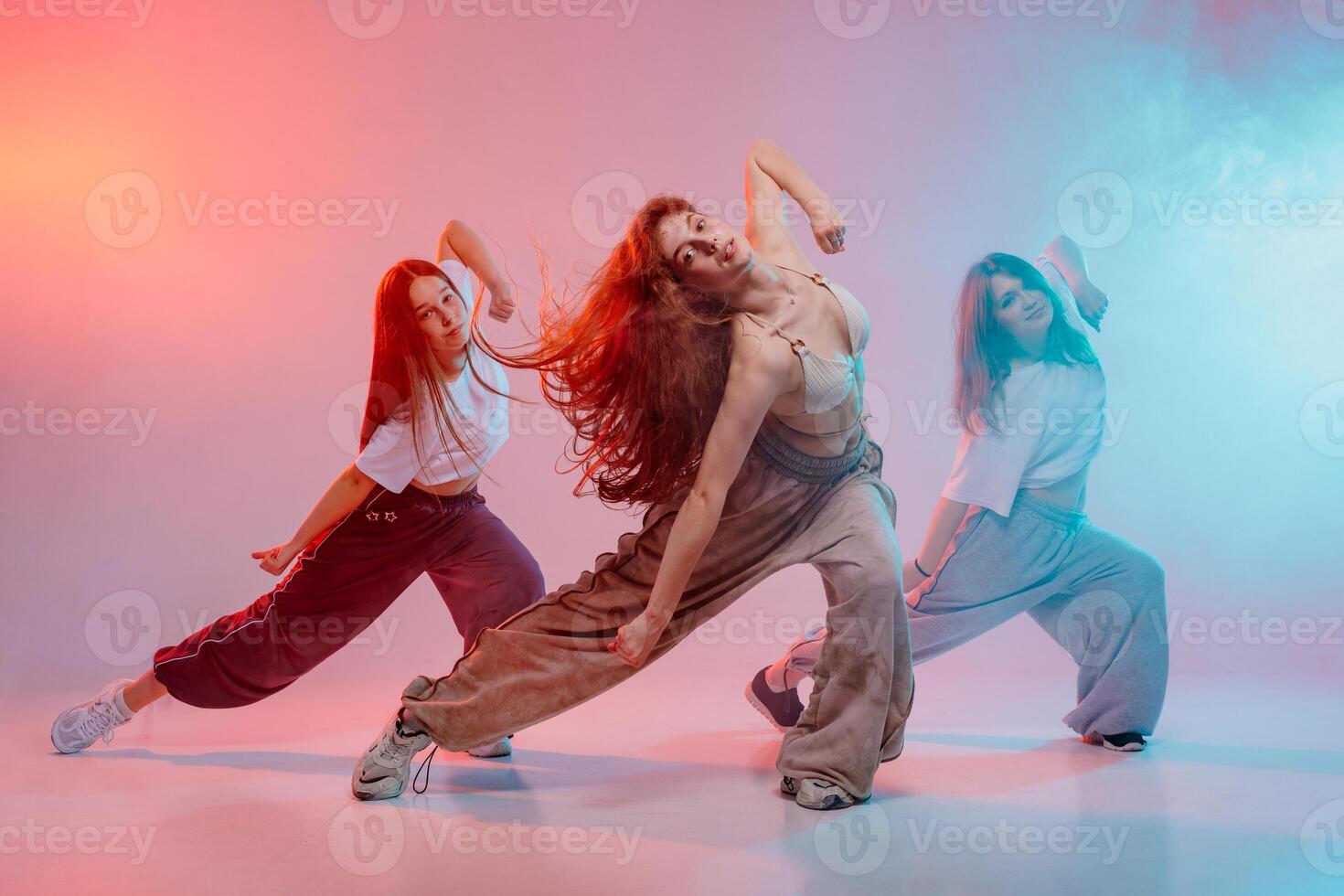 Three Young Women Dancing Jazz Funk in Studio with Expressive Moves and Colorful Modern Lighting photo