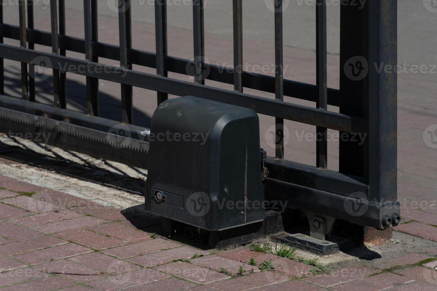 Automated sliding iron gate and motor on a brick driveway photo