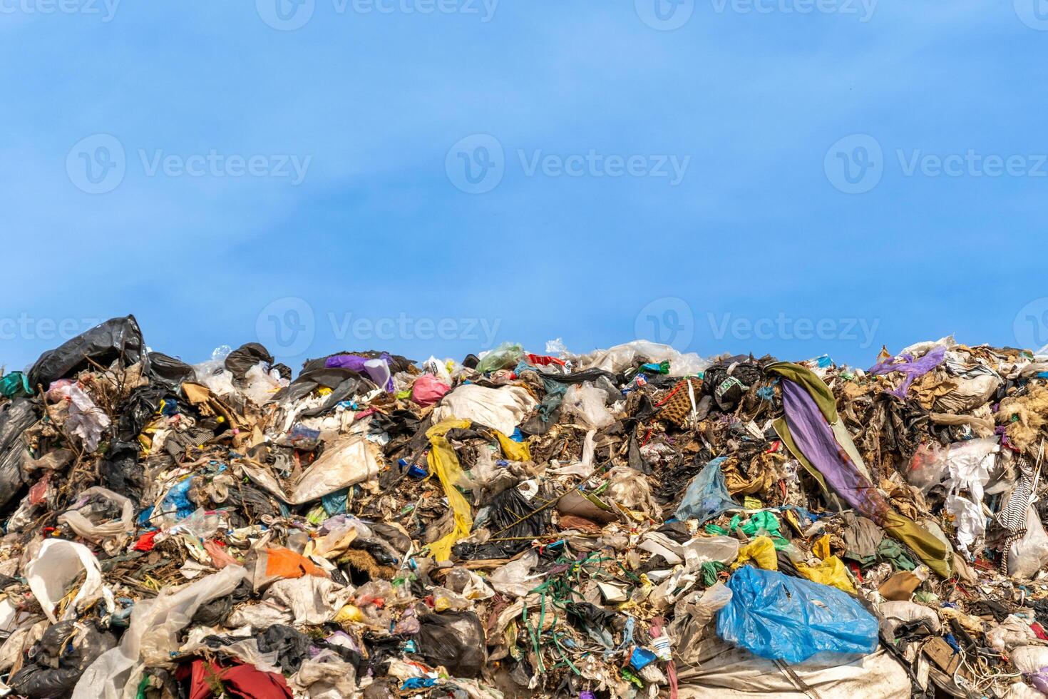 Massive Pile of Waste Overflowing in a Landfill with Plastic Bags and Discarded Materials under Blue Sky photo