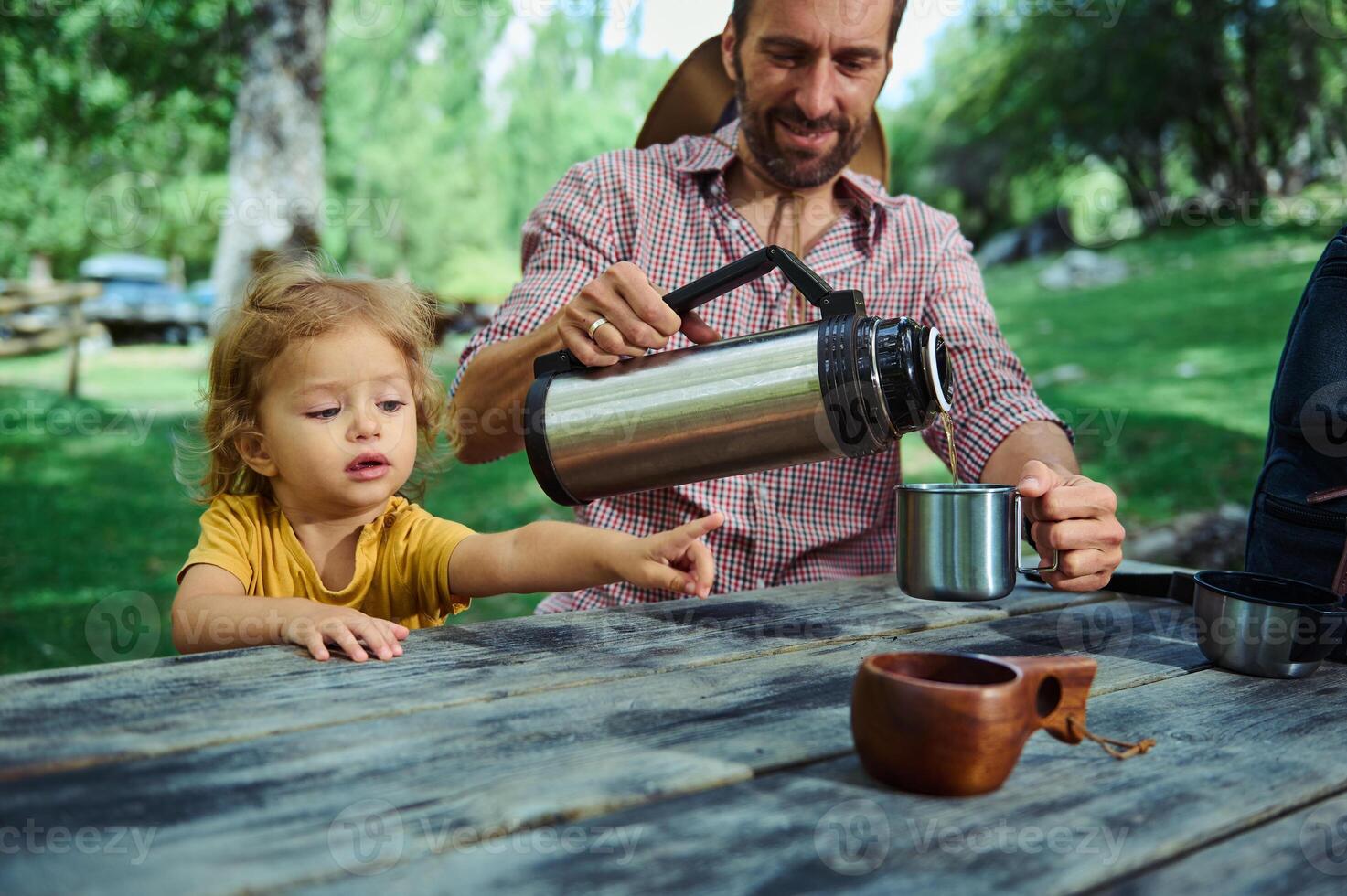 Father and Young Child Sharing Outdoor Bonding Moment Over Hot Beverage in Park Setting photo