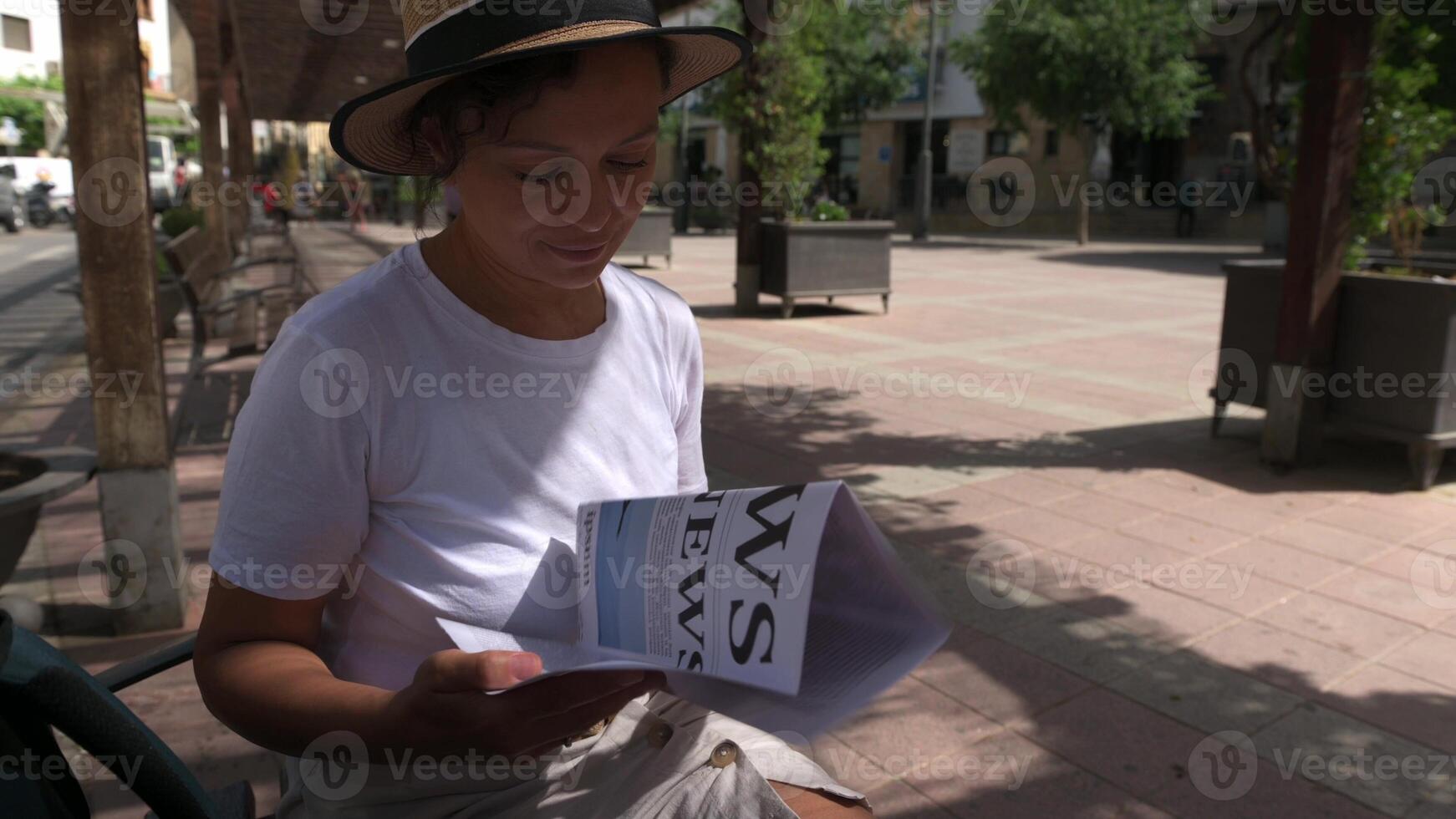 Curious Female Tourist Sits In A Sunny Old Town Square, Engaged In Reading A Paper Map To Explore The Historic City, photo