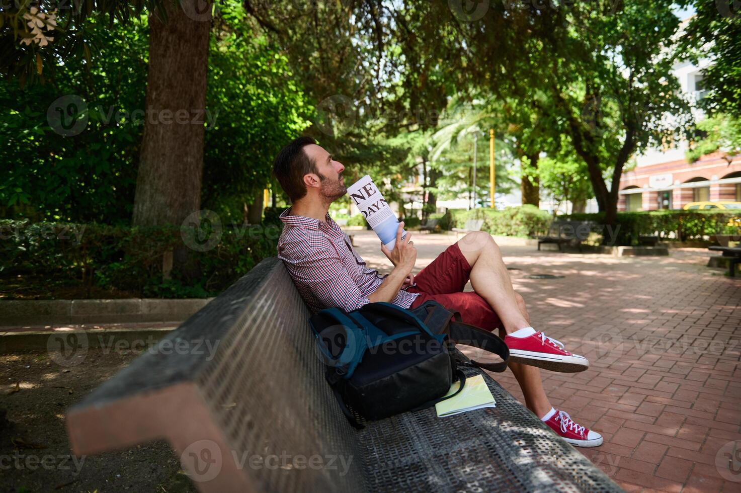 Man Relaxing on a Bench Reading a Newspaper in a Peaceful Park photo