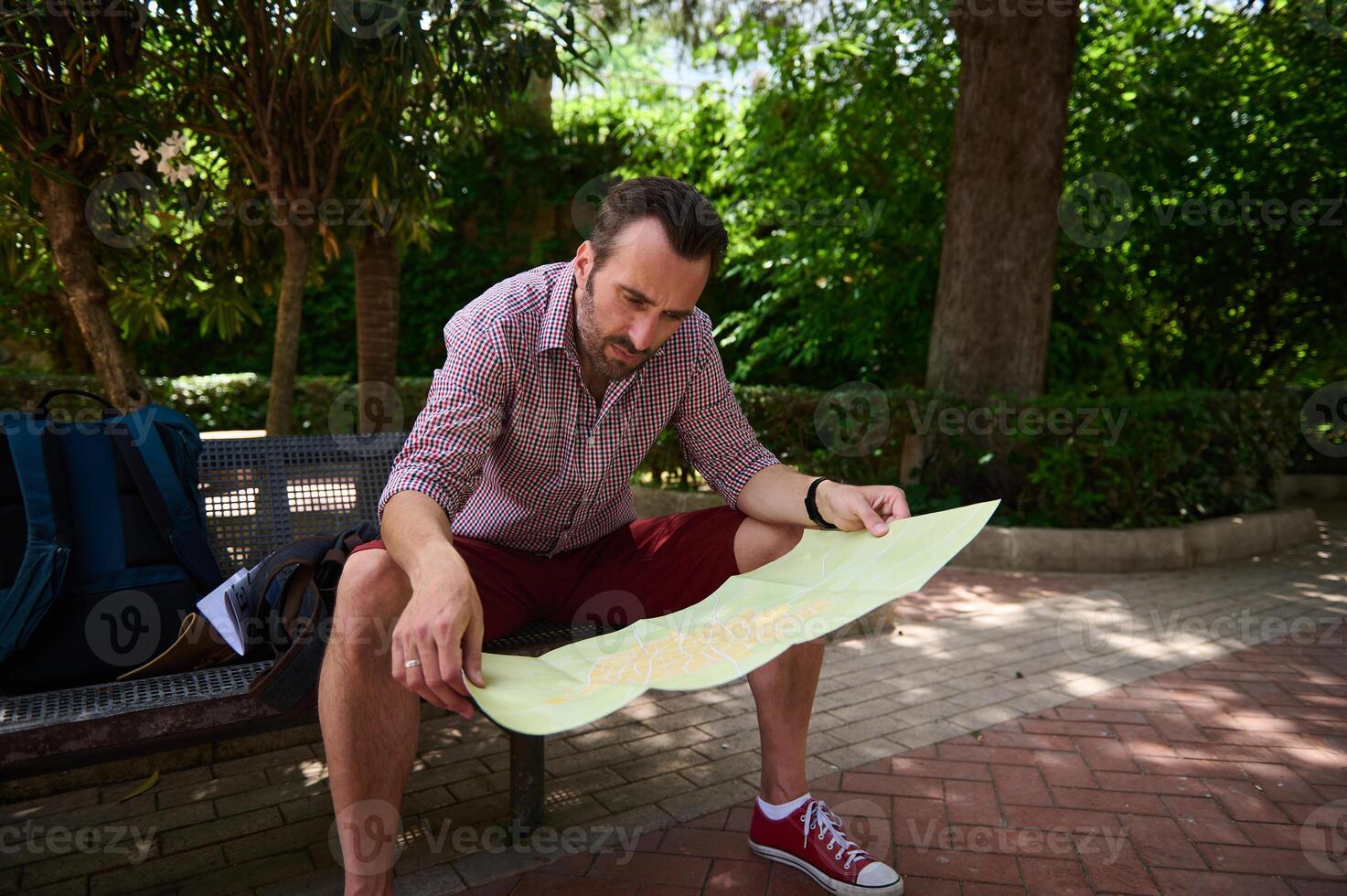 Man Sitting on Park Bench Studying Tourist Map in a Green Urban Area photo