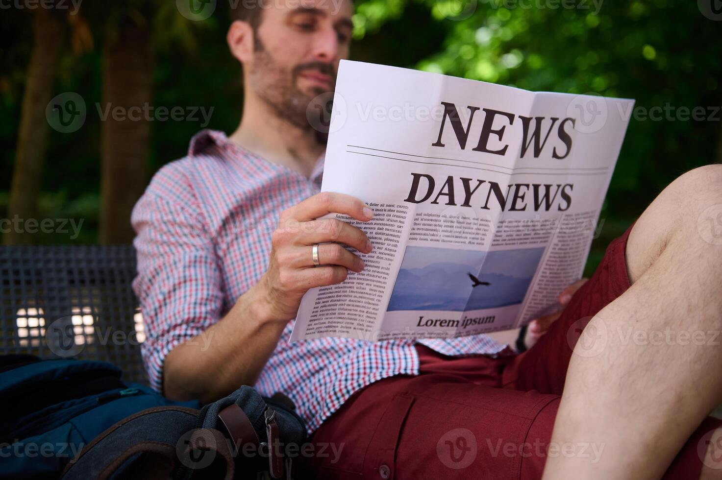 Man Sitting Outdoors Reading a Newspaper in the Park Surrounded by Green Trees photo