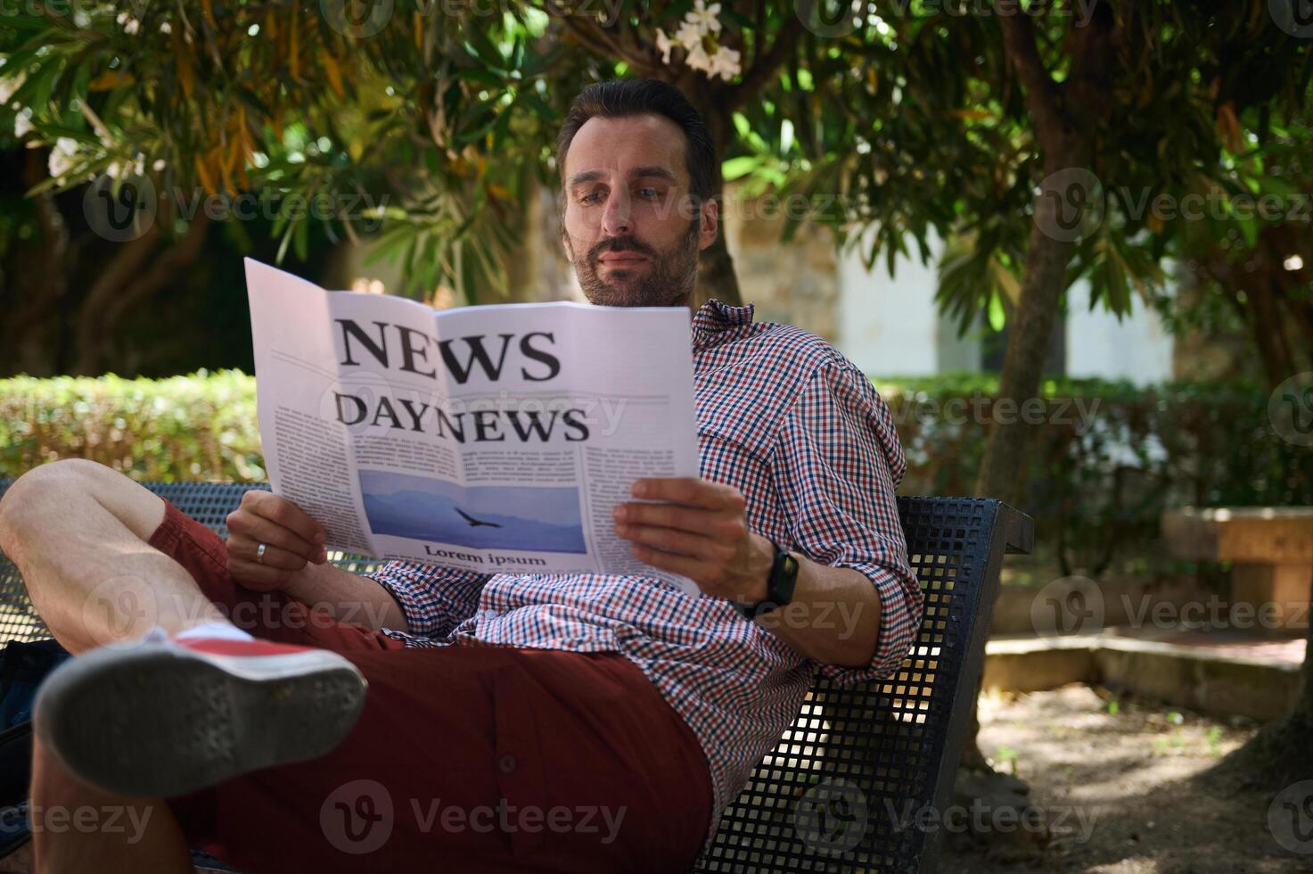 Man Relaxing in a Park and Reading a Newspaper Under Tree Shade on a Sunny Day photo