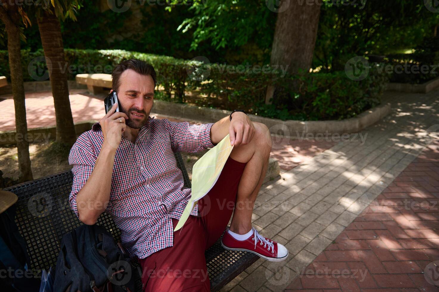 Man Sitting on a Bench in a Park Using a Phone and Reading a Map photo