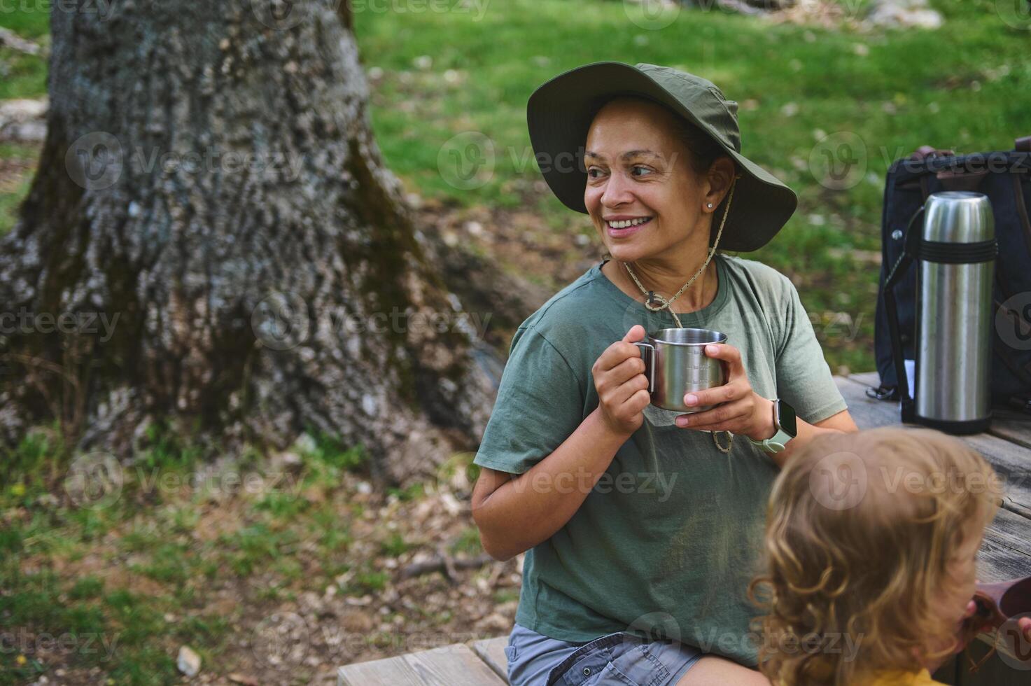 Smiling Woman Enjoying Coffee Outdoors with Child in a Scenic Park Setting photo