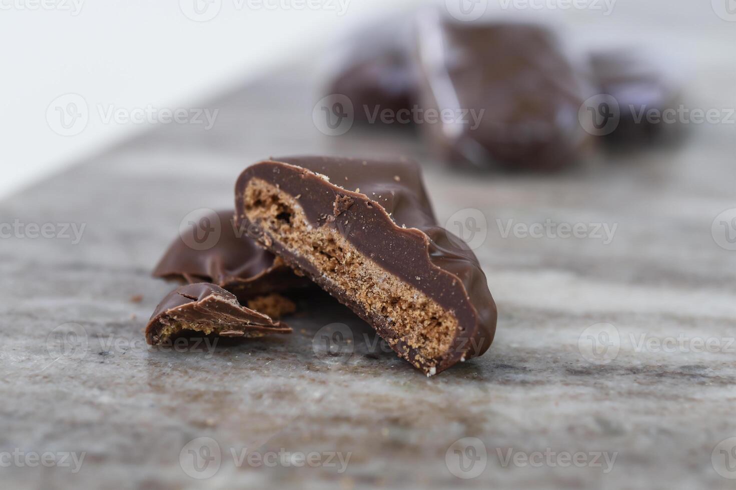 Decadent Chocolate Covered Biscuit Piece, broken in half to clearly show its textured, crumbly interior with hick layer of chocolate coating isolated on marble side view of sweet treat photo