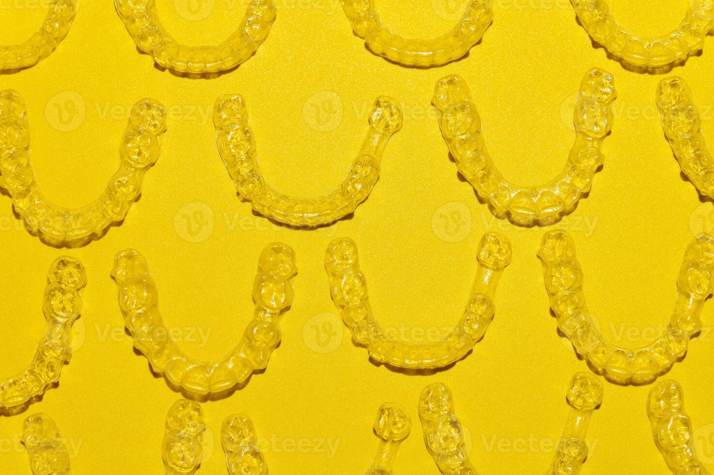 Clear dental aligners on colored yellow background, close-up side view from above. Pattern of clear braces photo