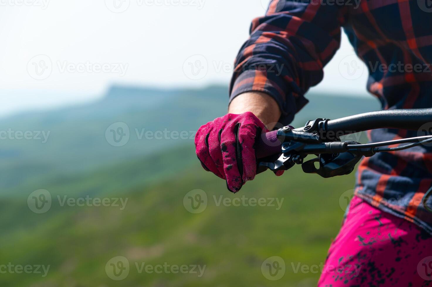 Close-up of mountain mtb bike handlebars against a mountain landscape in defocus. Rider's hand on the handlebars. Mountain downhill cycling. Copy space background for cycling photo