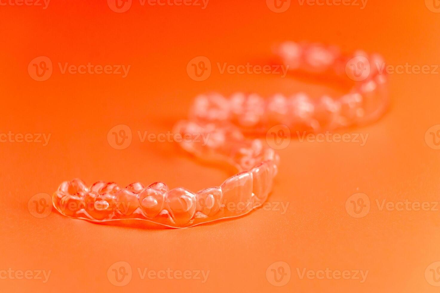 Invisible teeth retainers lie on a bright orange background. Close-up of a modern way to straighten teeth photo