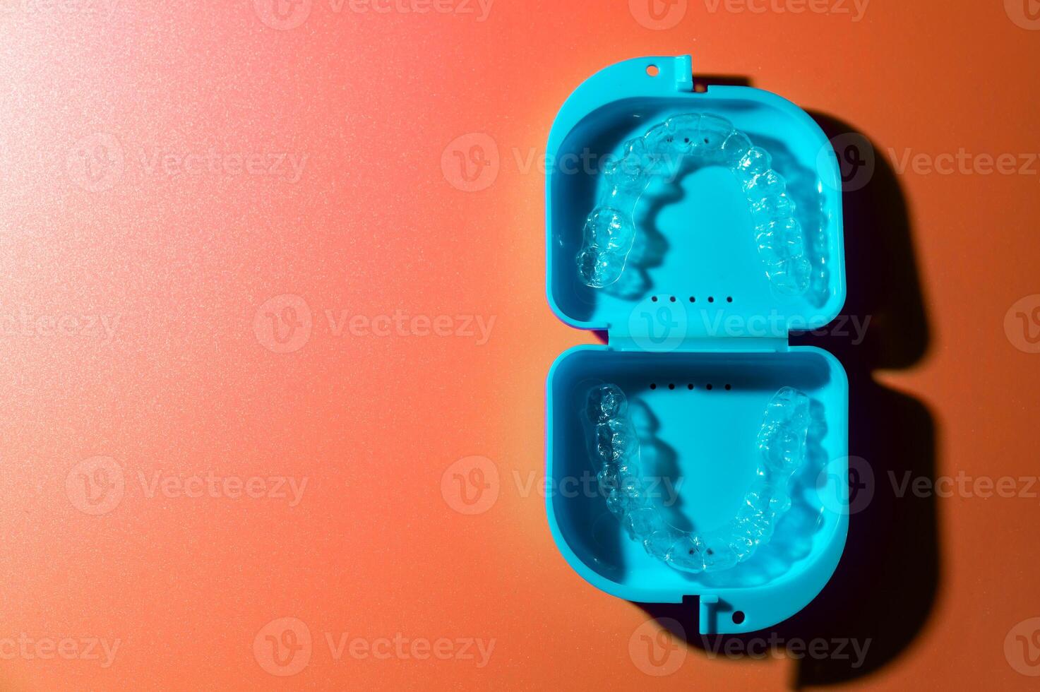 Blue plastic case with transparent brackets on a peach background. Invisible removable retainers for orthodontic treatment photo