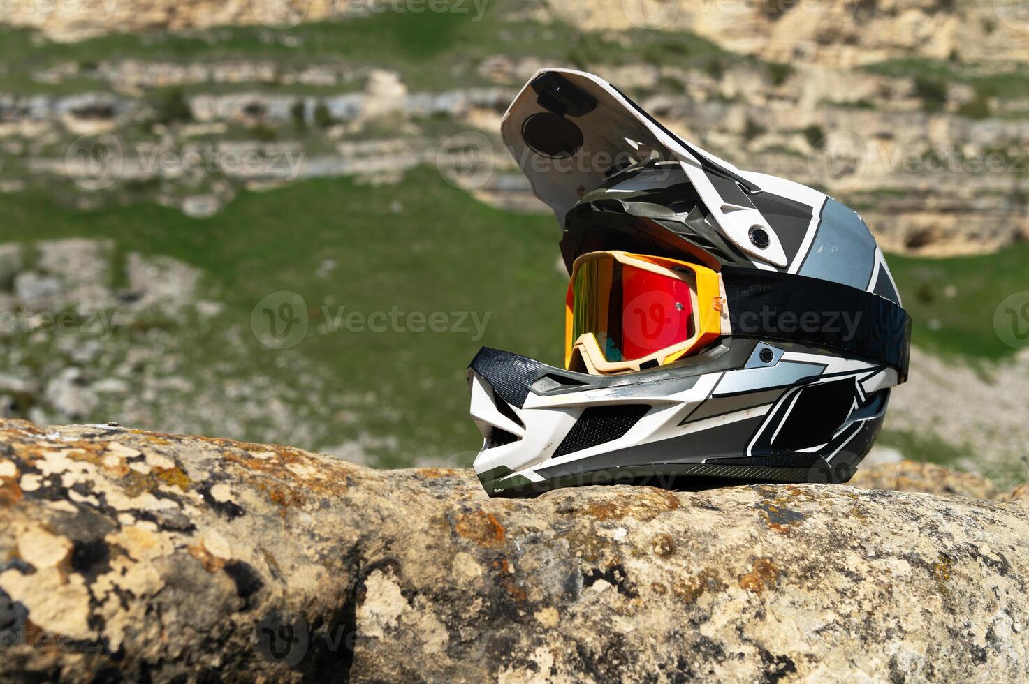 Professional full face helmet with goggles mask lies on a rock against the backdrop of a mountain landscape in the mountains on a sunny day. Used helmet for mountain biking and moto sports. photo