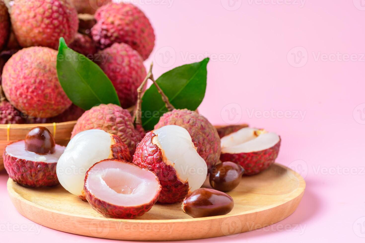Juicy Lychee with cut in half and leaves on wood plate isolated on pink background. Thai fruits photo