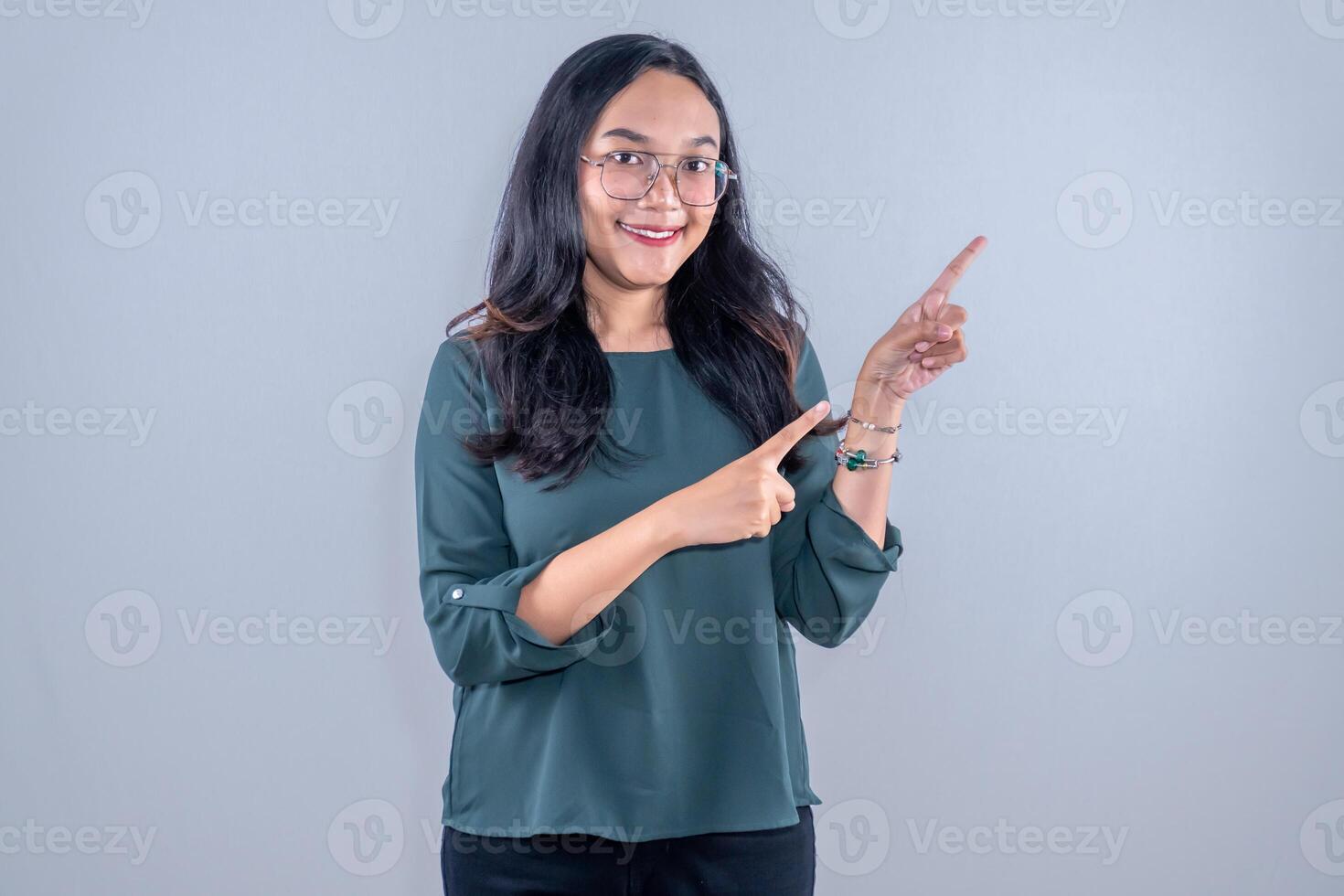 Indonesian Asian woman wearing green shirt with glasses smiling and pointing to the side photo