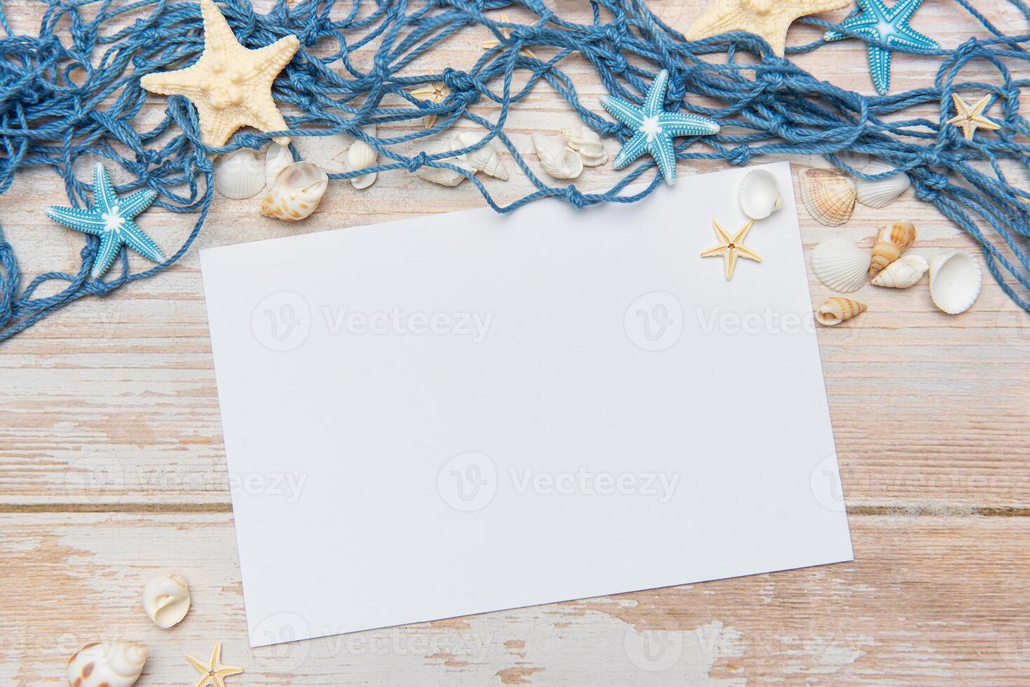 Fishing net, seashells and starfishes framing blank paper on wooden background photo