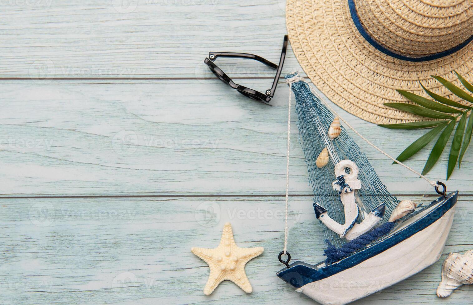Seashells, sunglasses, straw hat, starfish and decorative sailboat creating summer holiday atmosphere on wooden plank photo