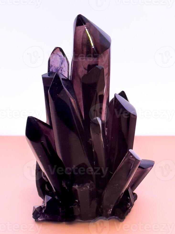 A striking, eye-level close-up captures a raw, deep purple amethyst crystal cluster, showcasing its natural facets and sharp points. The translucent mineral stands prominently against a soft, light photo