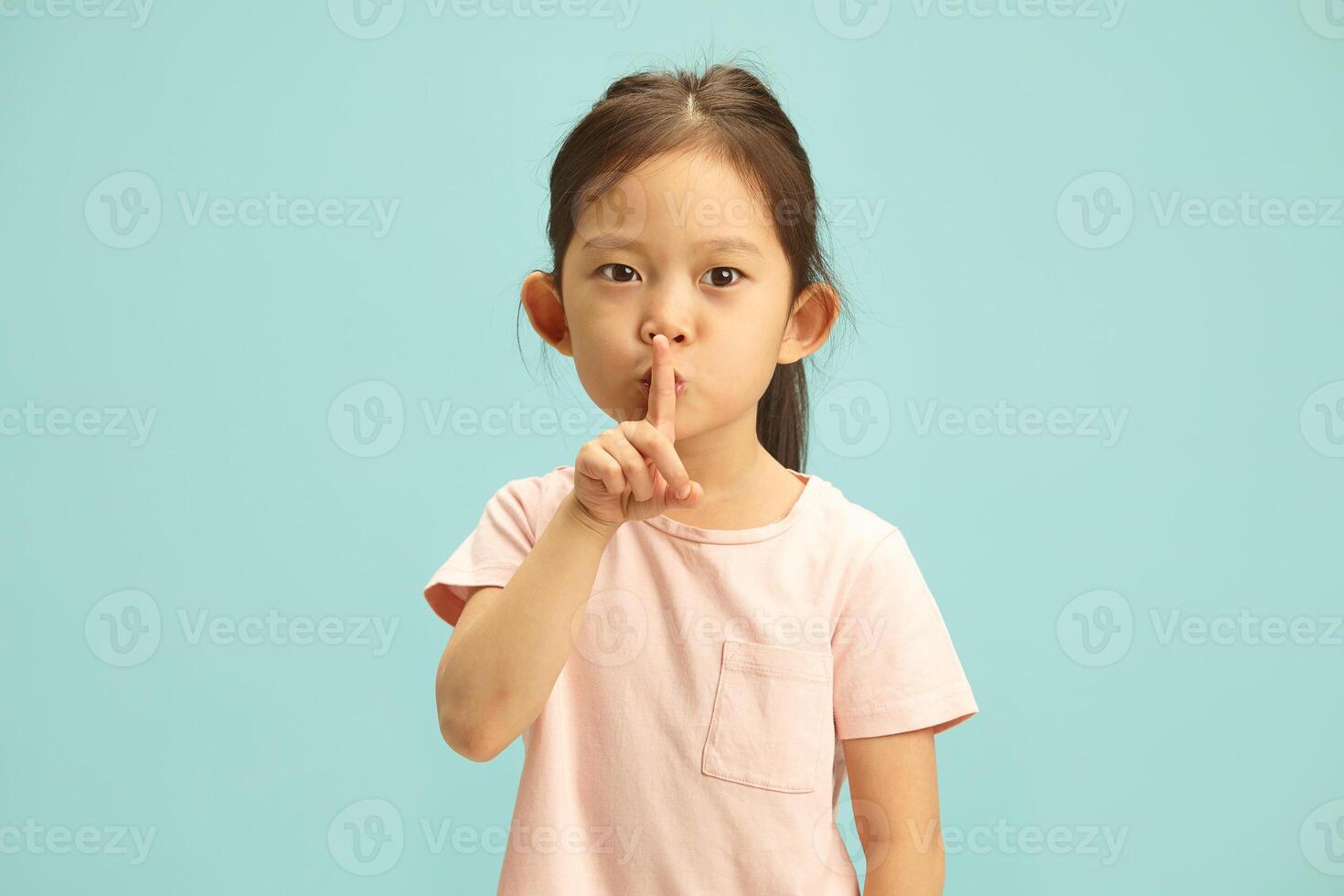 Serious little cute kid asking for silence and quiet, gesturing with finger in front of mouth, saying shh or keeping a secret standing against blue isolated background photo