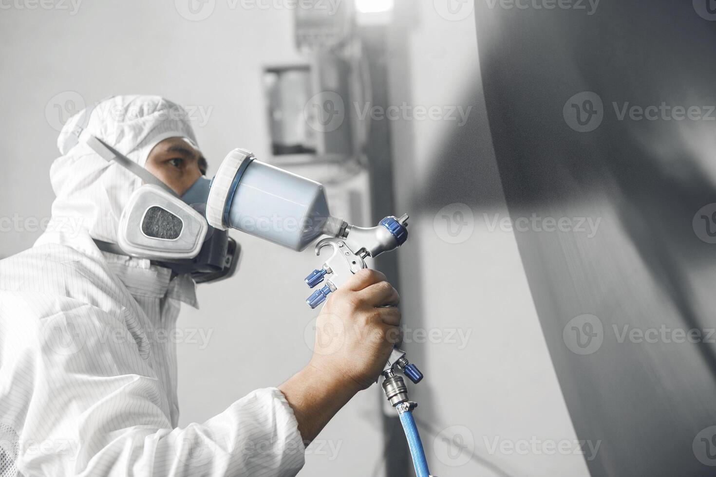 Close up shot of automobile repairman painter in mask and protective workwear painting part of car in paint chamber. photo