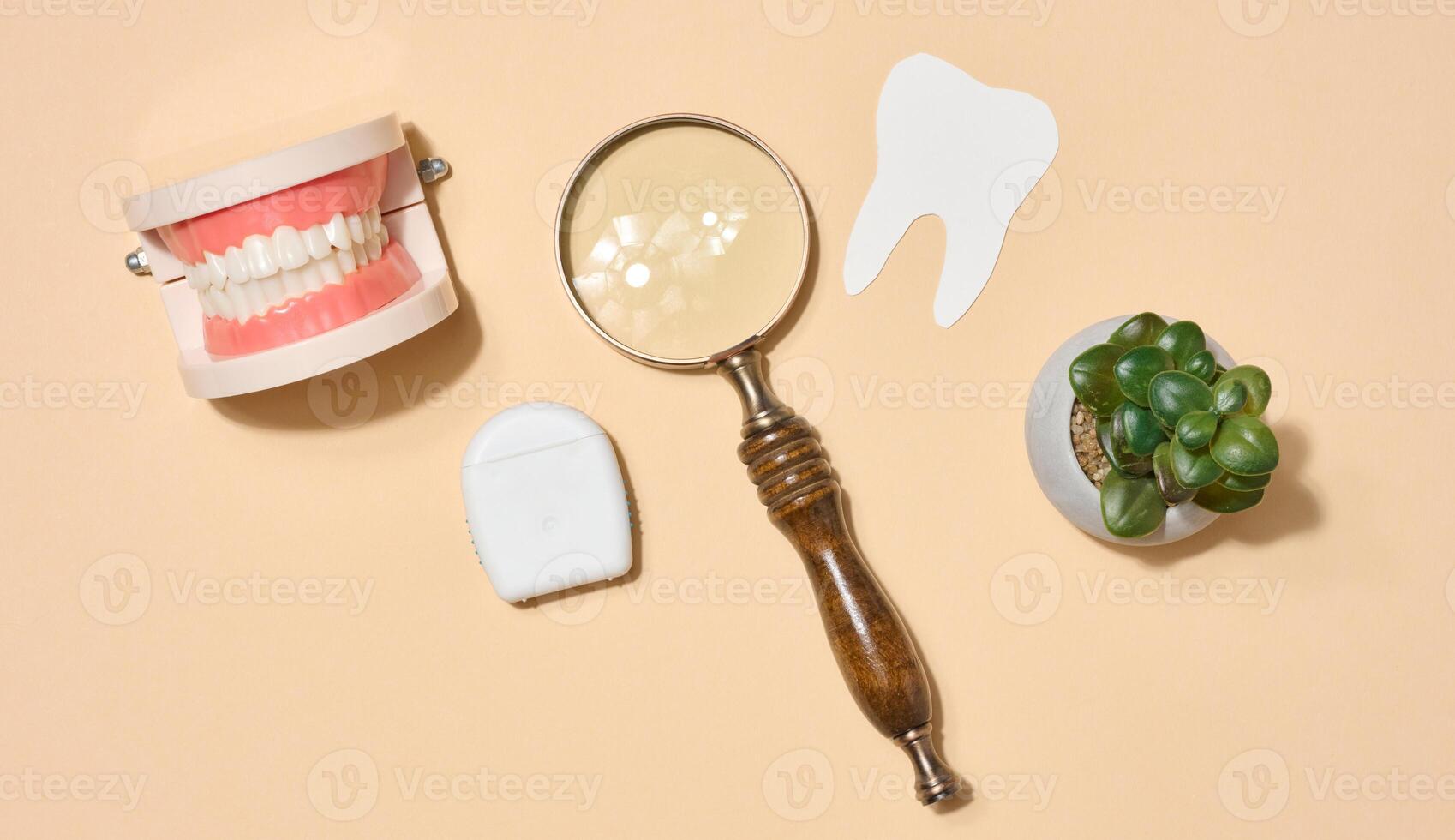 Model of dentures, magnifying glass located on beige background. Top view photo