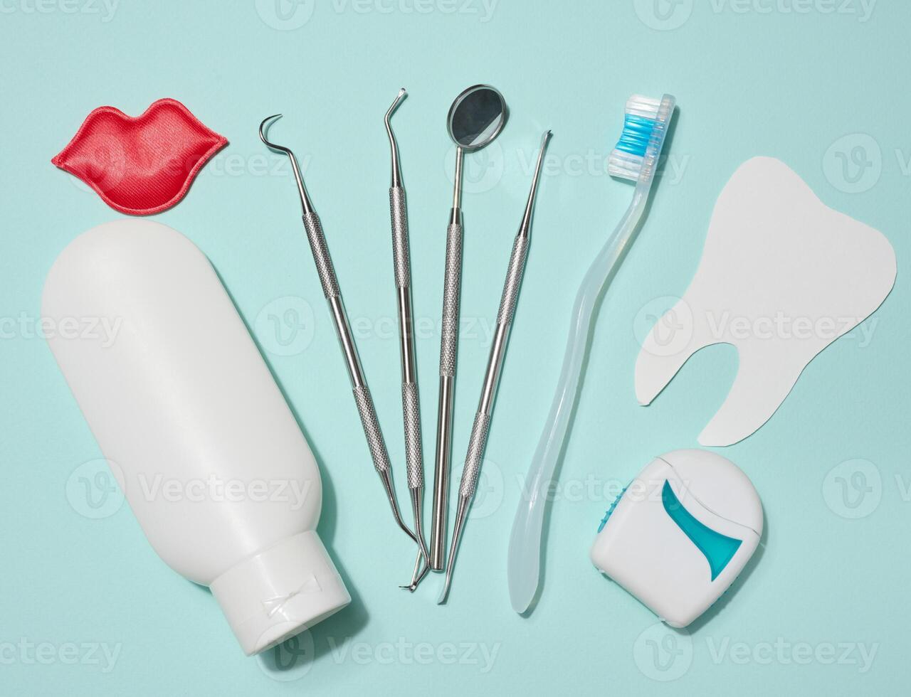 Red decorative lips, white tube of toothpaste, dental floss in white case, dental instruments and paper cut out white teeth on blue background. photo