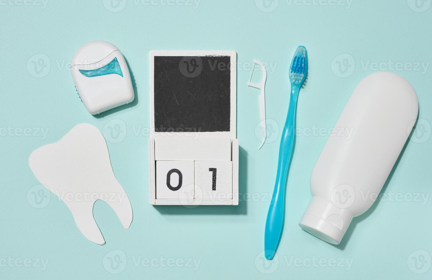 Blue toothbrush, white tube of toothpaste, dental floss in blue case and wooden calendar, paper teeth arranged on blue background. photo
