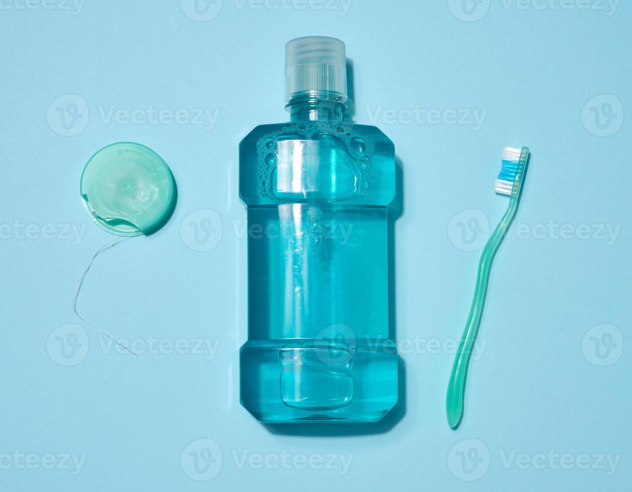 Bottle of blue mouthwash, dental floss in a blue case and green toothbrush placed on a blue background. Top view. photo