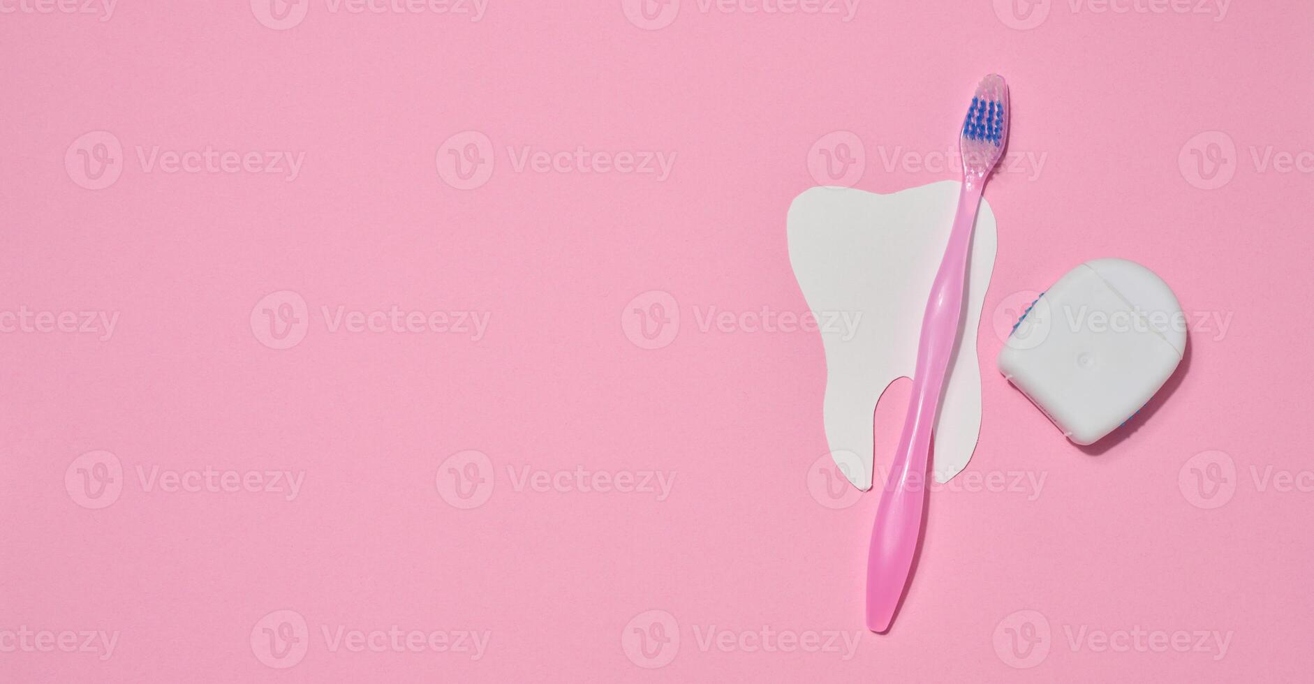 Pink toothbrush, dental floss in a case and a paper cutout tooth placed on a pink background. photo