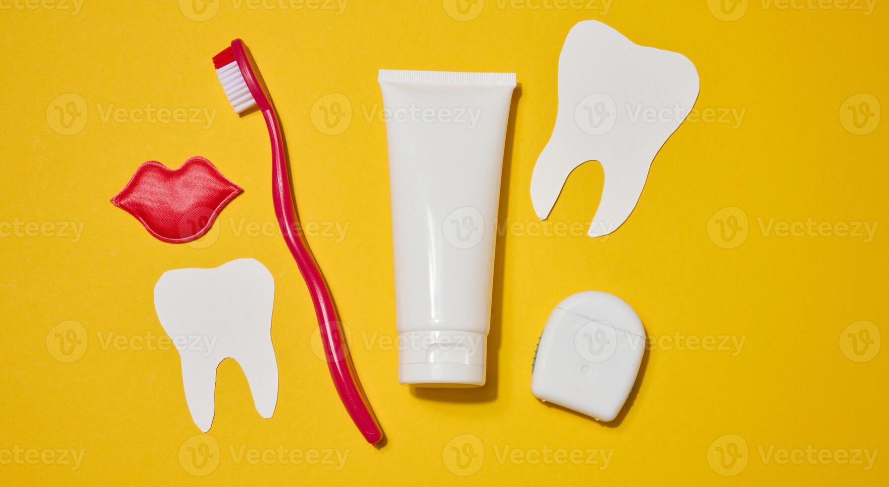 Red toothbrush, white tube of toothpaste, red decorative lips, dental floss in a case and a white paper tooth cut out on a bright yellow background. photo