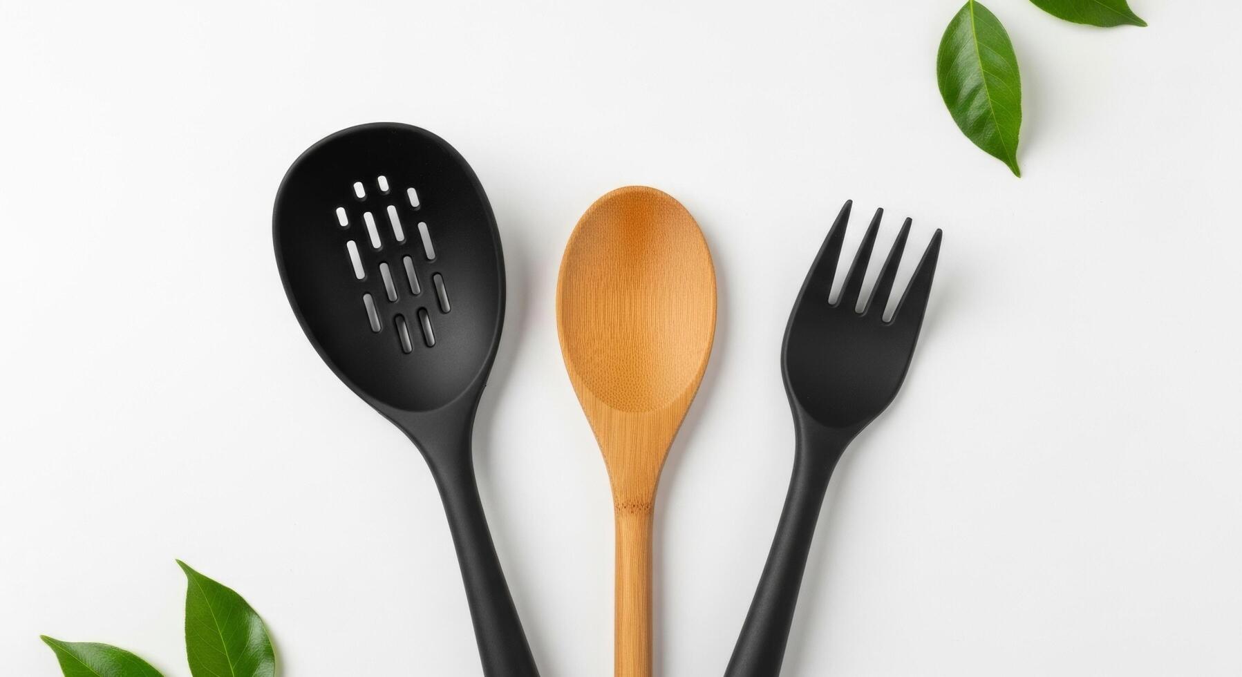 Kitchen Utensils Black Slotted Spoon, Wooden Spoon, and Black Fork with Green Leaves photo