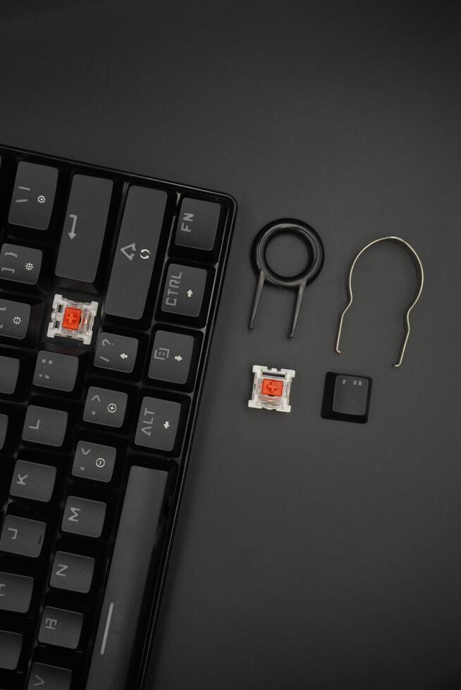 A black mechanical keyboard with a 61 layout with keycaps and switch puller and red switches on the side with a black background photo