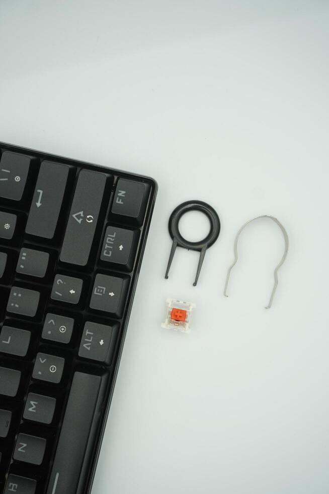 A black mechanical keyboard with keycaps puller and switch puller and red switches on the side with a white background. photo