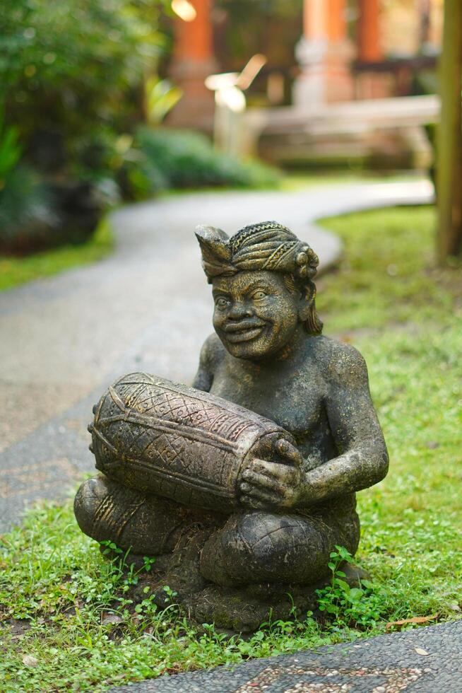 A stone carved to resemble a Balinese man playing a drum is the outdoor decoration of an inn in close up mode photo