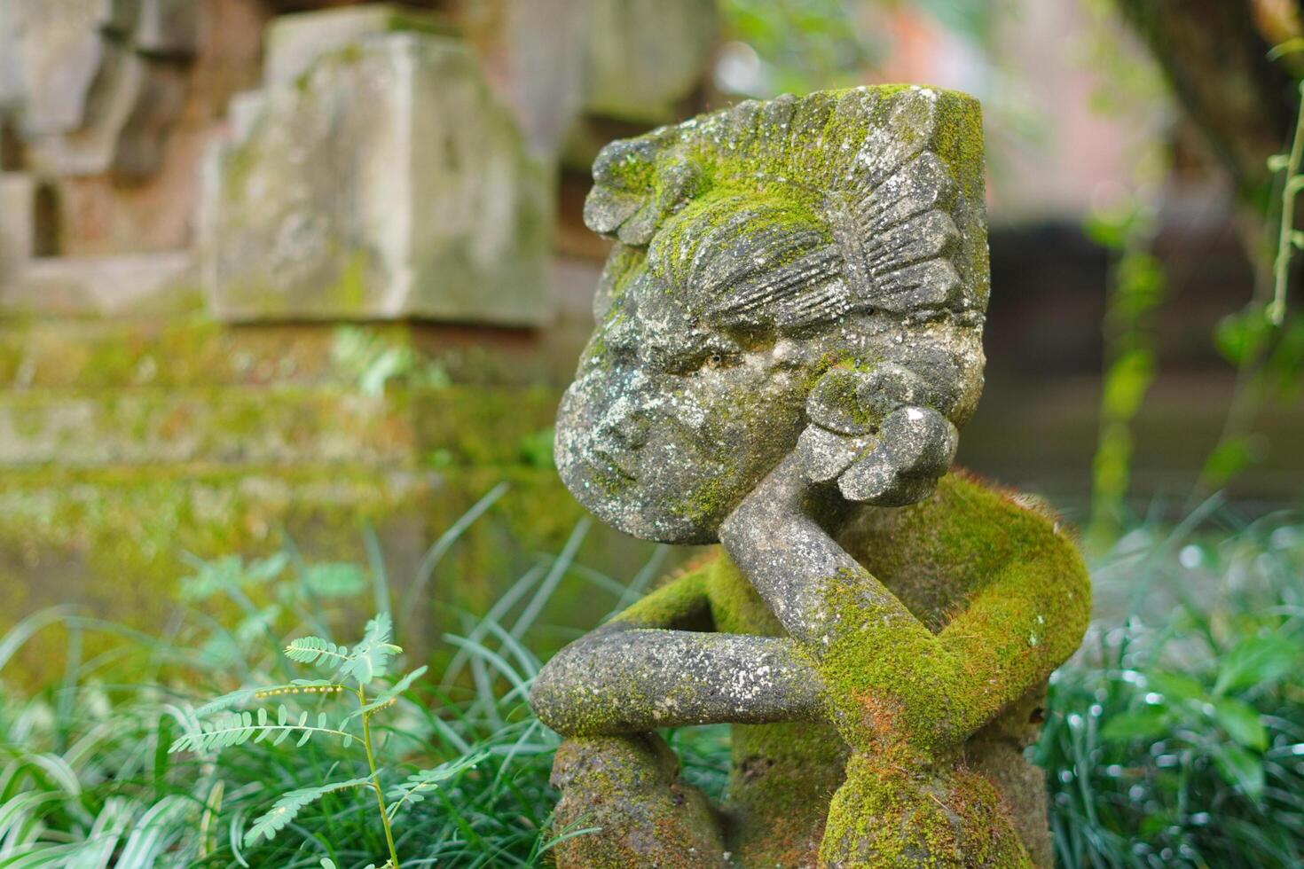 A statue carved from stone posing like a person supporting his chin while sitting with a Balinese concept photo
