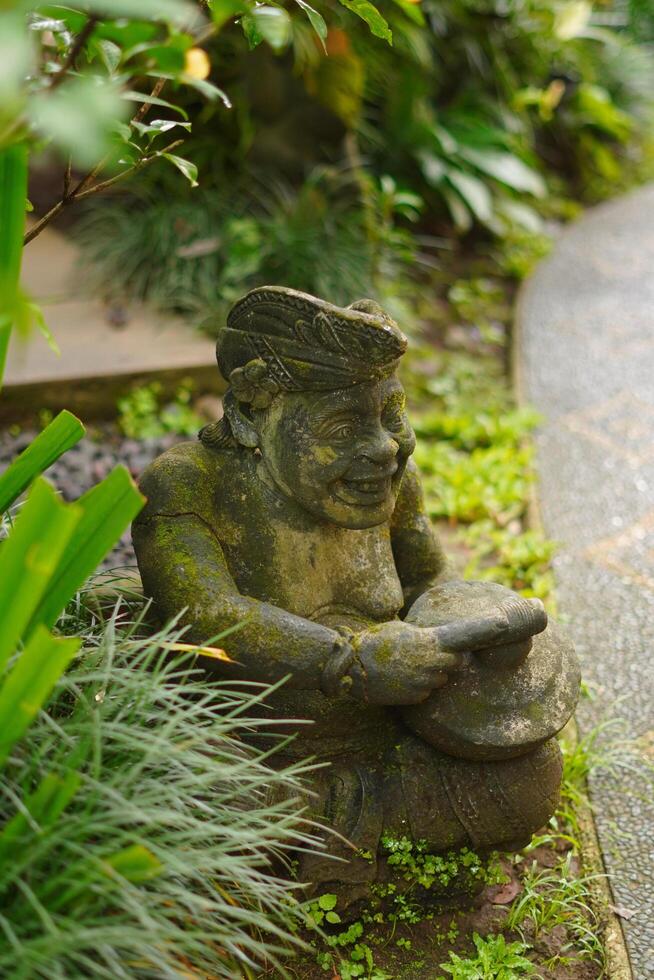 A statue carved from stone with a typical Balinese concept located among the leaves of trees. photo