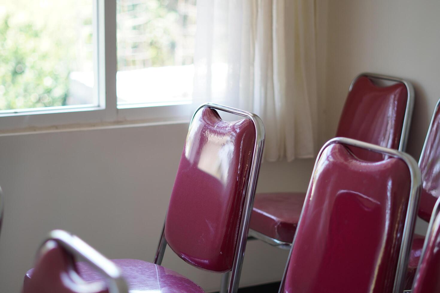Red chairs lined up near a window in a room during the day photo