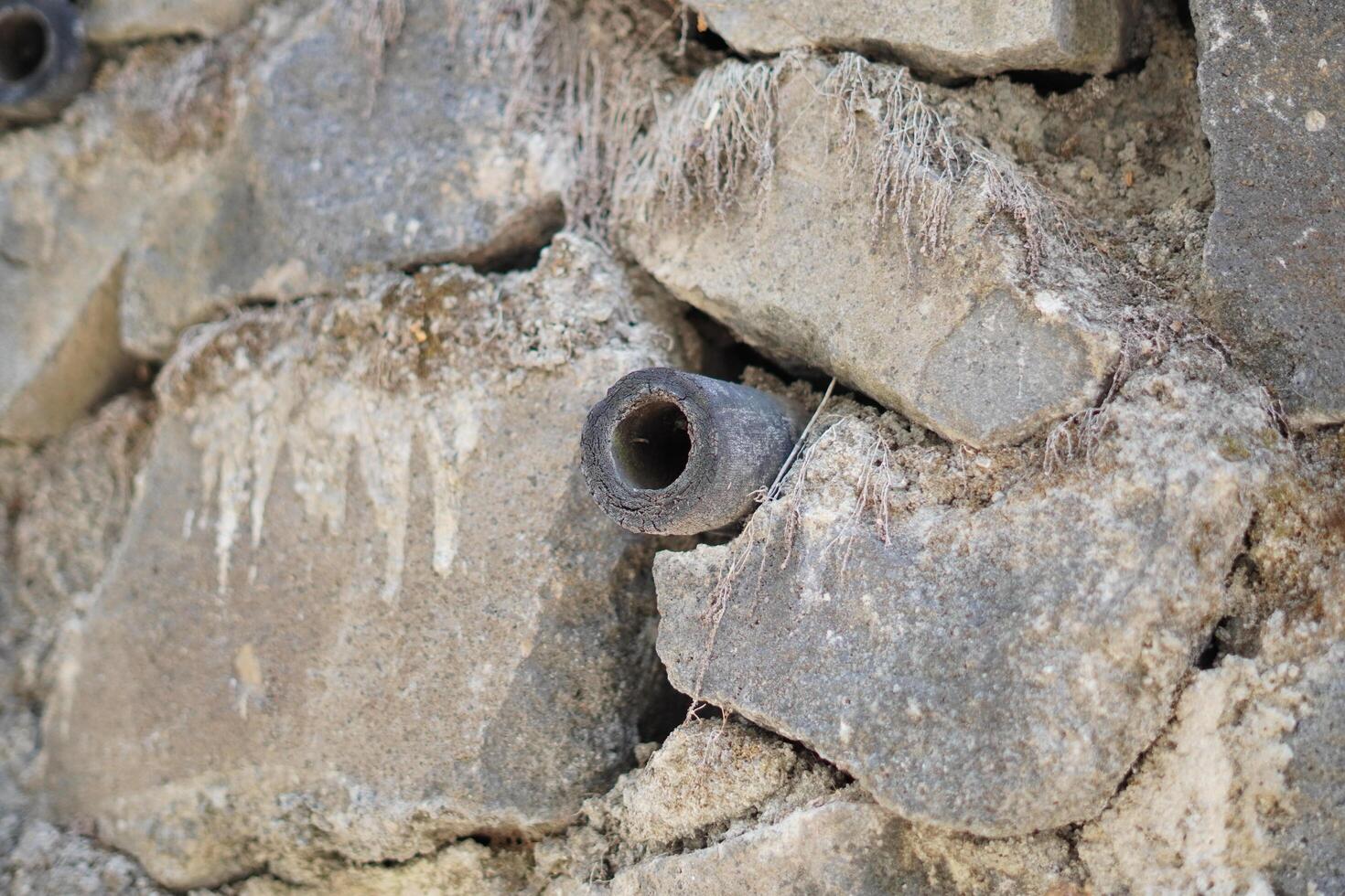 A small pipe in the middle of a wall made of piles of stones with hole photo