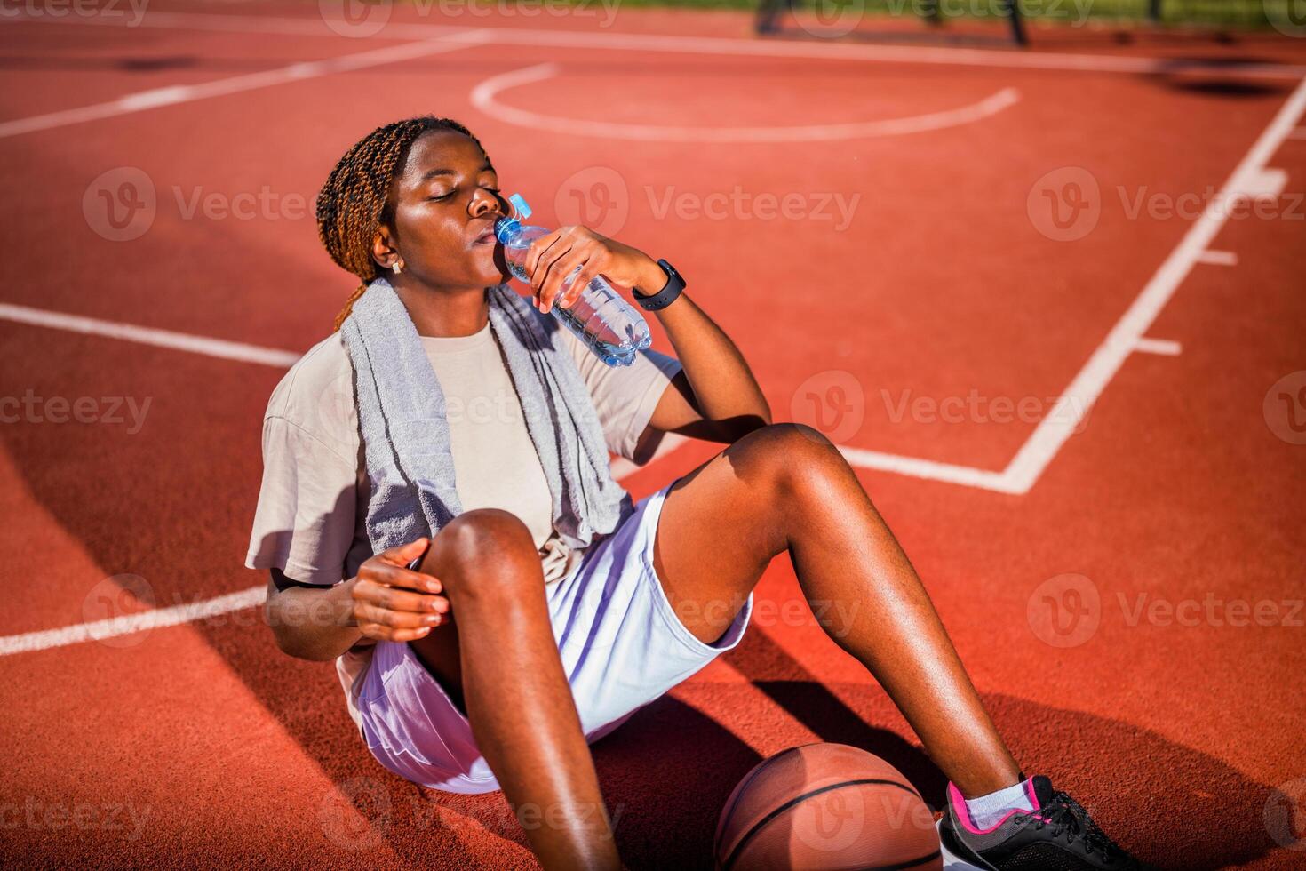Young black woman practicing basketball alone at sports court in the morning. She is exhausted and drinking water. photo